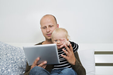 Vater, der zu Hause bleibt, benutzt ein Tablet, während er seinen kleinen Sohn hält - FOLF05998