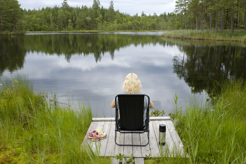 Frau sitzt auf Steg am Seeufer, lizenzfreies Stockfoto