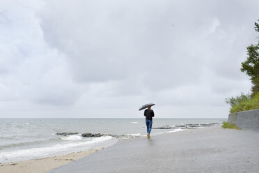 Frau unter schwarzem Regenschirm spazierend am Strand - FOLF06015