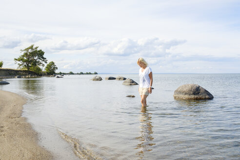 Frau watet im Wasser am Strand eines Sees - FOLF06024