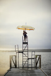 Frau mit Regenschirm auf Leiter stehend am See - FOLF06182