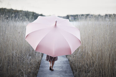 Woman with umbrella walking on wooden pier - FOLF06185