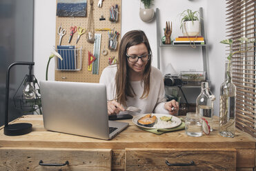 Woman having lunch at wooden table with laptop - SKCF00378