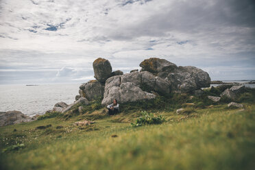 Frankreich, Bretagne, Landeda, Dunes de Sainte-Marguerite, junge Frau sitzt an Felsen an der Küste - GUSF00573