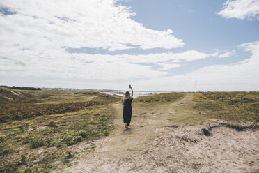 Frankreich, Bretagne, Landeda, Dunes de Sainte-Marguerite, junge Frau geht auf einer Düne an der Küste spazieren und hält ein Handy in der Hand - GUSF00580