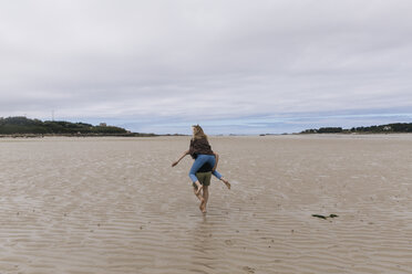 Frankreich, Bretagne, Guisseny, junger Mann läuft mit Freundin huckepack am Strand - GUSF00584