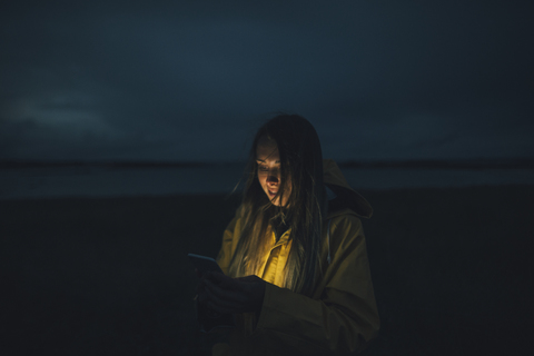 Frankreich, Bretagne, Landeda, Dunes de Sainte-Marguerite, Frau benutzt Handy am Strand bei Nacht, lizenzfreies Stockfoto