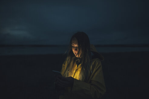 Frankreich, Bretagne, Landeda, Dunes de Sainte-Marguerite, Frau benutzt Handy am Strand bei Nacht - GUSF00593