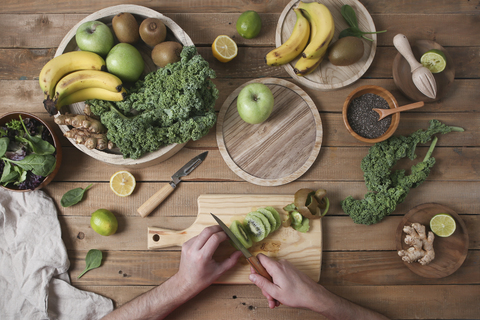 Mann bereitet grünen Smoothie zu und schneidet Kiwi, lizenzfreies Stockfoto