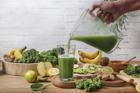 Man serving glass of green smoothie surrounded by ingredients - RTBF01125