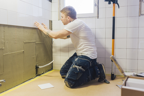 Fliesenleger beim Anbringen von Fliesen an der Wand in einem Badezimmer, lizenzfreies Stockfoto