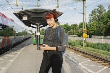 Woman wearing headphones on train platform - FOLF06277