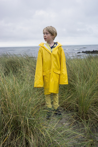 Junge im Tussockgras am Strand in Regenkleidung, lizenzfreies Stockfoto