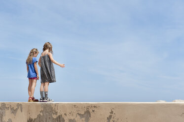 Rückansicht von zwei jungen Mädchen, die an einer Mauer stehen - FOLF06492
