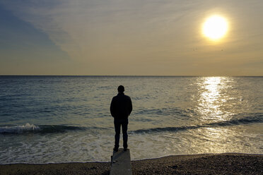 Italy, Liguria, Riviera di Ponente, Noli, man standing at beach at sunrise - LBF01875
