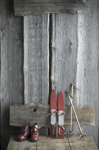 Alte Kinderskier, Skistöcke und Skischuhe stehen auf einer Holzbank, lizenzfreies Stockfoto