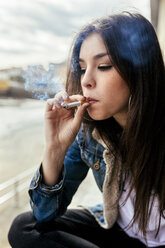 Junge Frau raucht eine Zigarette im Freien - MGOF03744