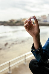 Hand einer Frau beim Rauchen einer Zigarette in einem Küstendorf - MGOF03745