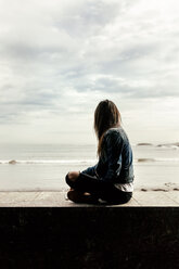 Young woman sitting on a wall looking at the sea - MGOF03747