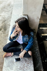 Young woman sitting on a wall smoking a cigarette - MGOF03748