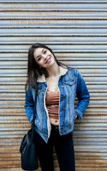 Portrait of a smiling young woman in front of a rusty metal blind - MGOF03750