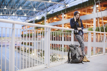 Glückliche Frau, die am Flughafen am Geländer lehnt und mit ihrem Handy telefoniert - CAVF32123