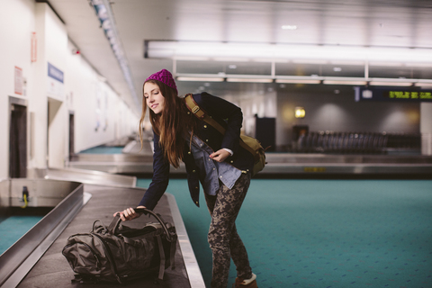 Frau trägt Gepäck aus der Gepäckausgabe am Flughafen, lizenzfreies Stockfoto