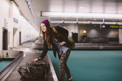 Woman carrying luggage from baggage claim at airport - CAVF32125