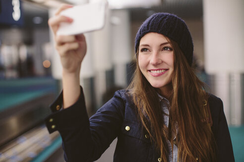 Happy woman taking selfie while standing at airport - CAVF32128