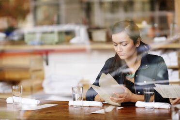 Frau, die im Restaurant sitzend die Speisekarte betrachtet, gesehen durch Glas - CAVF32131