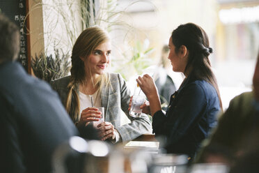 Female friends talking while having drinks by window in restaurant - CAVF32136