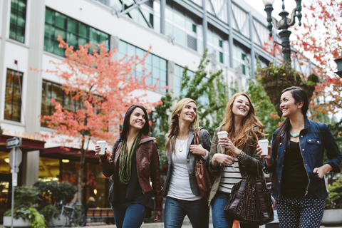 Fröhliche Freundinnen halten Kaffeetassen und unterhalten sich beim Spazierengehen auf der Straße, lizenzfreies Stockfoto