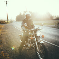 Männlicher Motorradfahrer auf dem Motorrad sitzend an der Straße gegen den Himmel an einem sonnigen Tag - CAVF32159