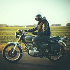 Porträt eines männlichen Motorradfahrers, der auf einer Landstraße gegen den Himmel fährt und dabei gestikuliert - CAVF32163