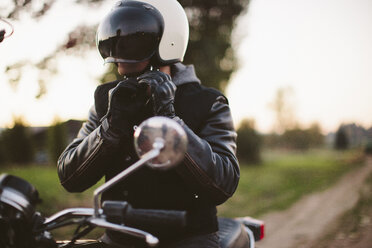 Männlicher Motorradfahrer passt seinen Helm an, während er auf dem Motorrad sitzt - CAVF32166