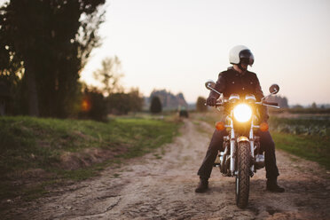 Männlicher Motorradfahrer auf einem unbefestigten Weg gegen den klaren Himmel bei Sonnenuntergang - CAVF32167