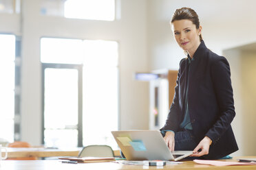 Porträt einer selbstbewussten Geschäftsfrau mit Laptop auf einem Tisch im Büro - CAVF32182