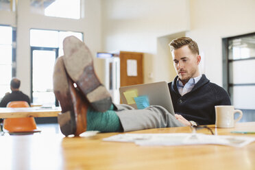 Businessman using laptop computer at desk in office while colleague working in background - CAVF32185