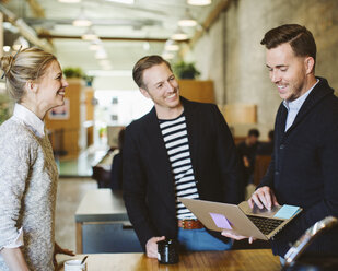 Businessman using laptop computer while standing with colleagues in office - CAVF32188