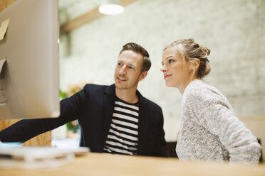 Geschäftsleute, die im Stehen im Büro auf einen Desktop-Computer schauen - CAVF32198