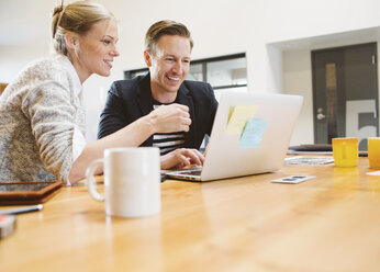 Smiling business people using laptop computer at desk in office - CAVF32220