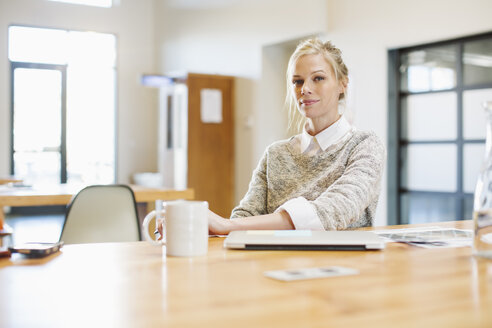 Porträt einer selbstbewussten Geschäftsfrau, die am Tisch mit einem Laptop im Büro sitzt - CAVF32224