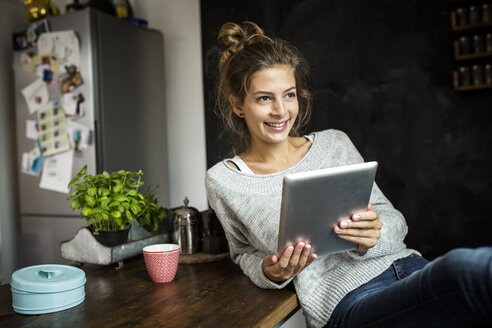 Smiling woman sitting at table holding tablet - PNEF00571