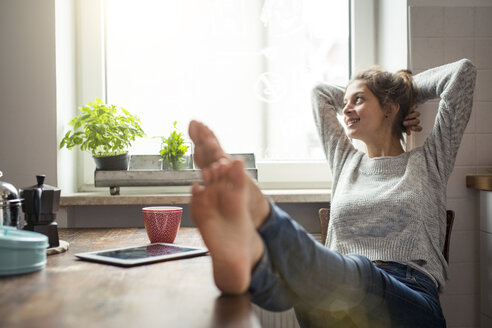 Woman sitting at table in kitchen relaxing - PNEF00572