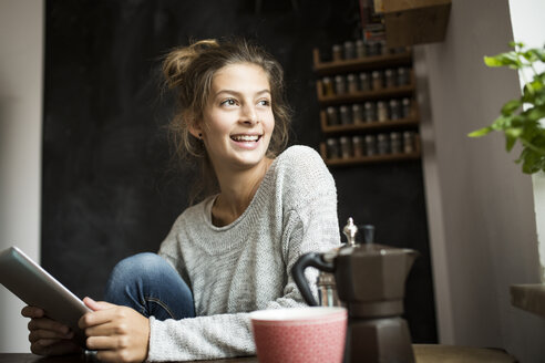 Smiling woman sitting at table holding tablet - PNEF00574