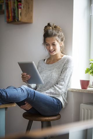 Lächelnde Frau sitzt auf einem Hocker und benutzt ein Tablet, lizenzfreies Stockfoto