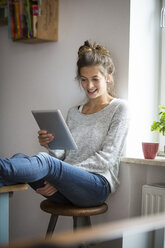 Smiling woman sitting on stool using tablet - PNEF00575