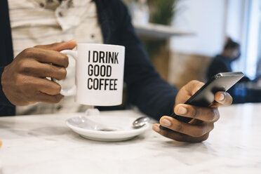 Nahaufnahme eines Mannes mit einer Tasse Kaffee in einem Café, der ein Mobiltelefon benutzt - MAUF01361