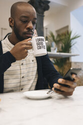 Mann mit einer Tasse Kaffee in einem Café, der ein Mobiltelefon benutzt - MAUF01362