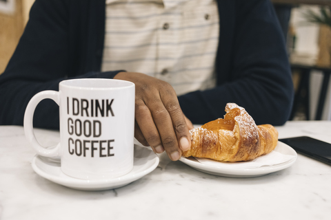 Nahaufnahme eines Mannes mit Croissant und Tasse Kaffee in einem Café, lizenzfreies Stockfoto